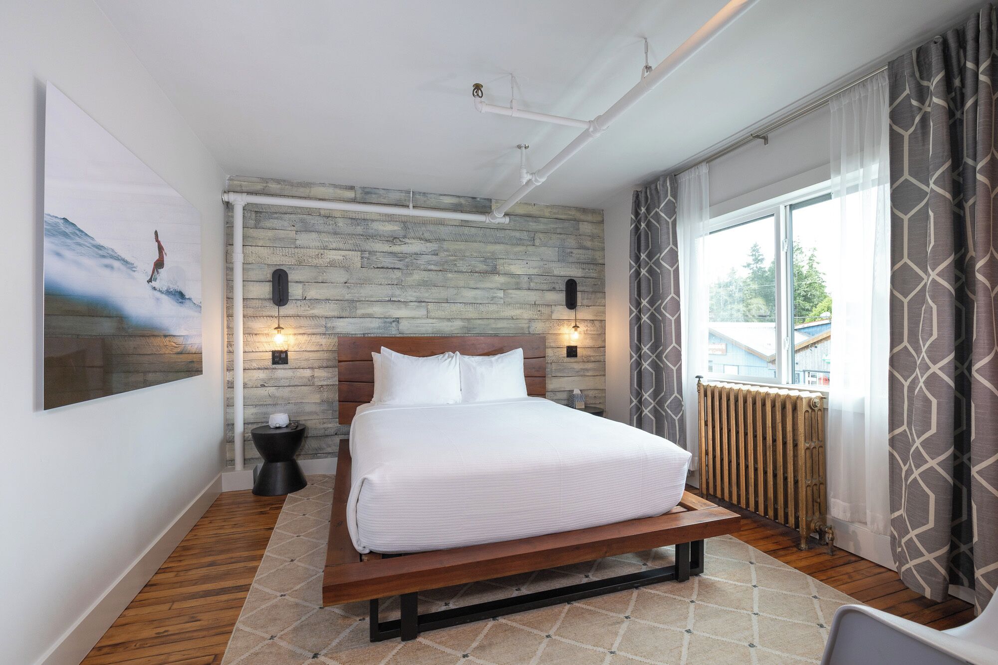 A bedroom with a wooden bed, a large window with curtains, and a wall-mounted light fixture.