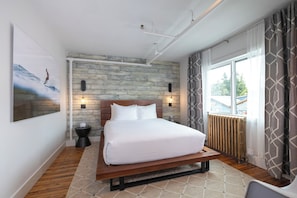 A bedroom with a wooden bed, a large window with curtains, and a wall-mounted light fixture. - The Maq Hotel (Tofino)