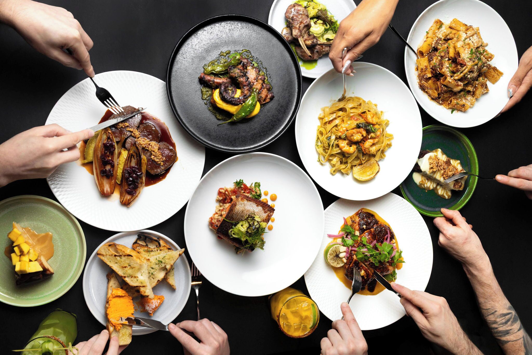 A variety of dishes on plates with people eating.