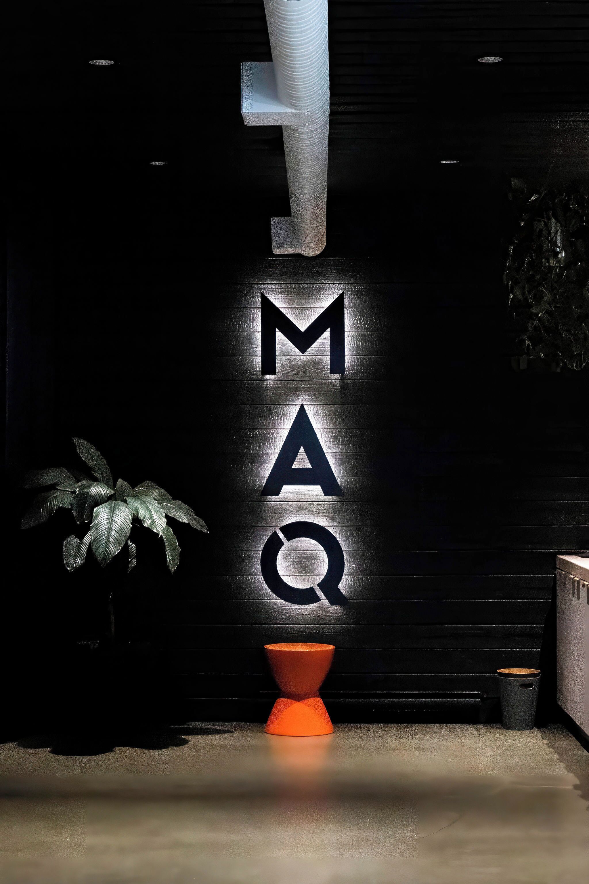 Un espace d’accueil avec une grande enseigne lumineuse portant l’inscription « MAQ ».