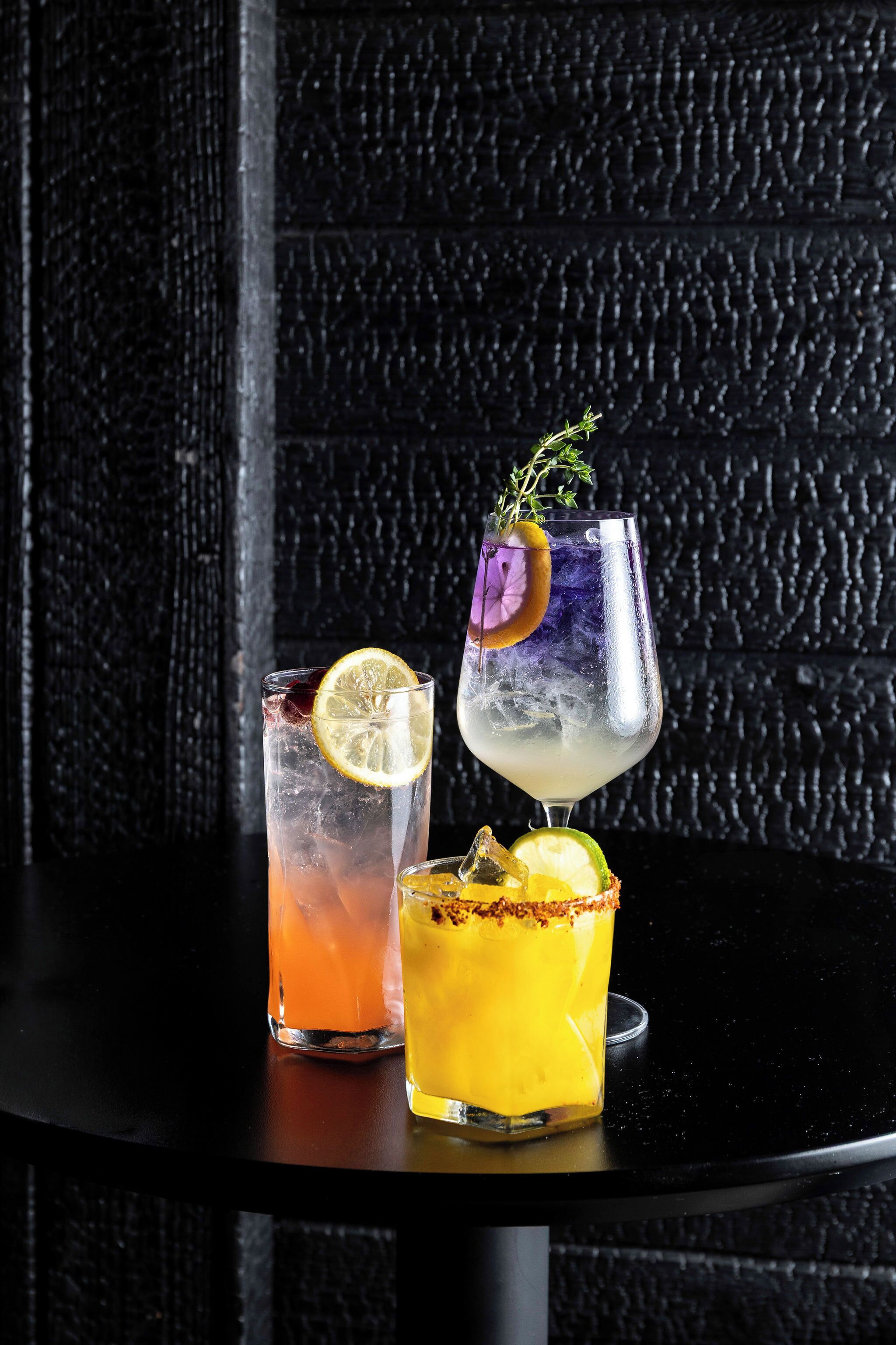 Tres vasos de bebidas sobre una mesa con un fondo negro texturizado.