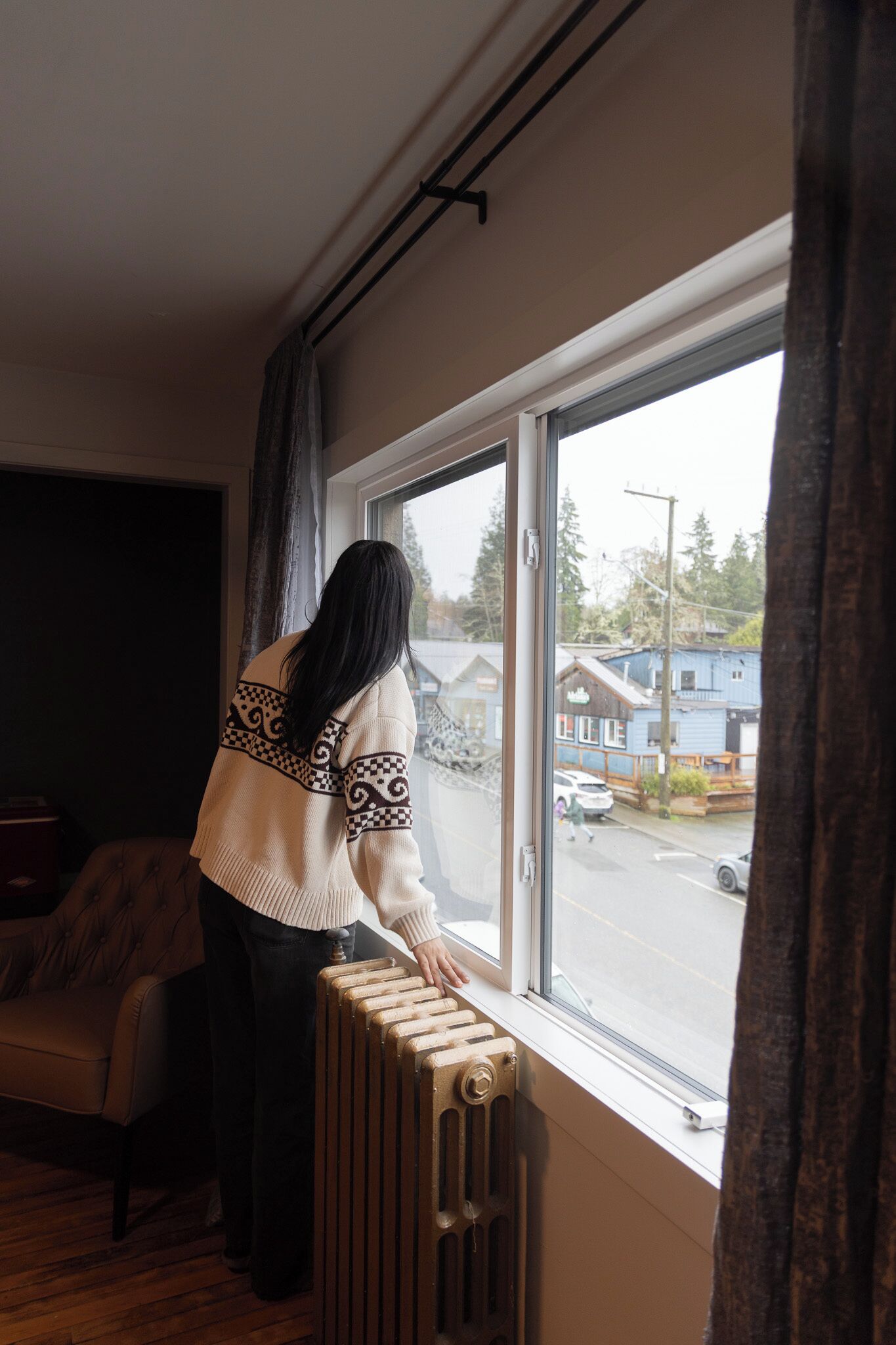 A person standing by a window with a view of a street and buildings.