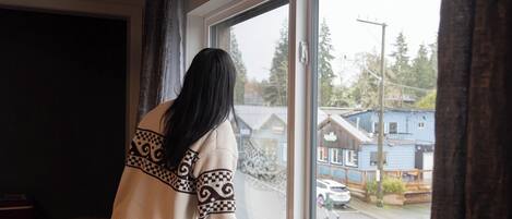 A person standing by a window with a view of a street and buildings.