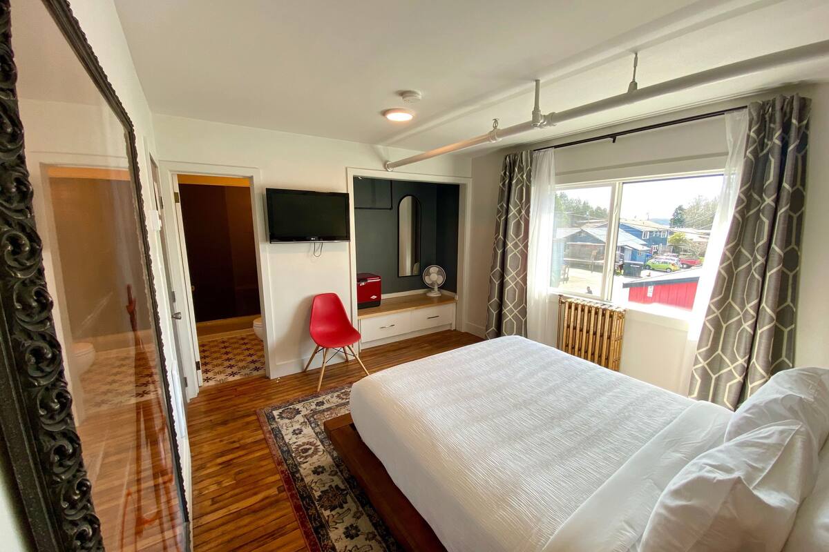 A hotel room with a bed, a TV, a red chair, and a window with curtains.