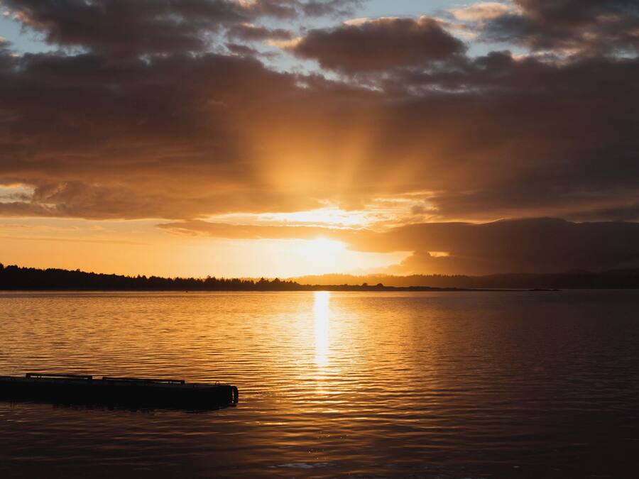 Un atardecer sobre aguas tranquilas con un muelle en primer plano.
