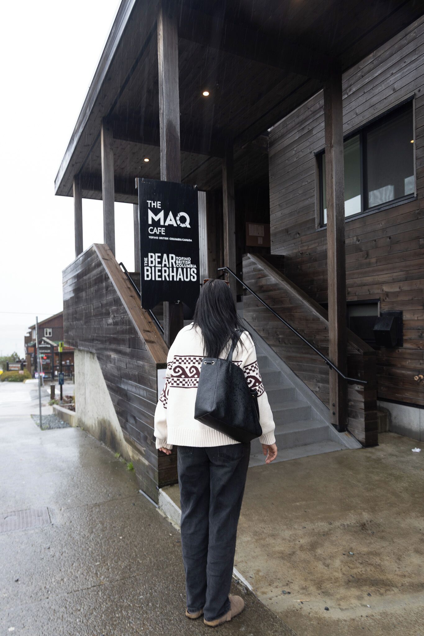 Una persona caminando hacia un edificio con un letrero que dice 'The Bear Bierhaus' y 'The MaQ Cafe'.