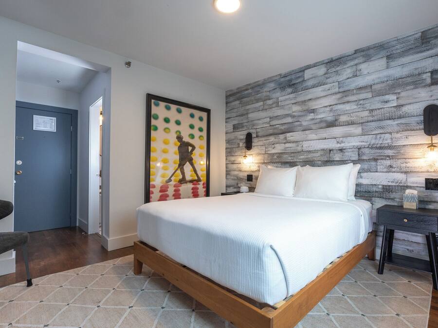Un dormitorio con cama, mesita de noche, lámpara de pared y una puerta.
