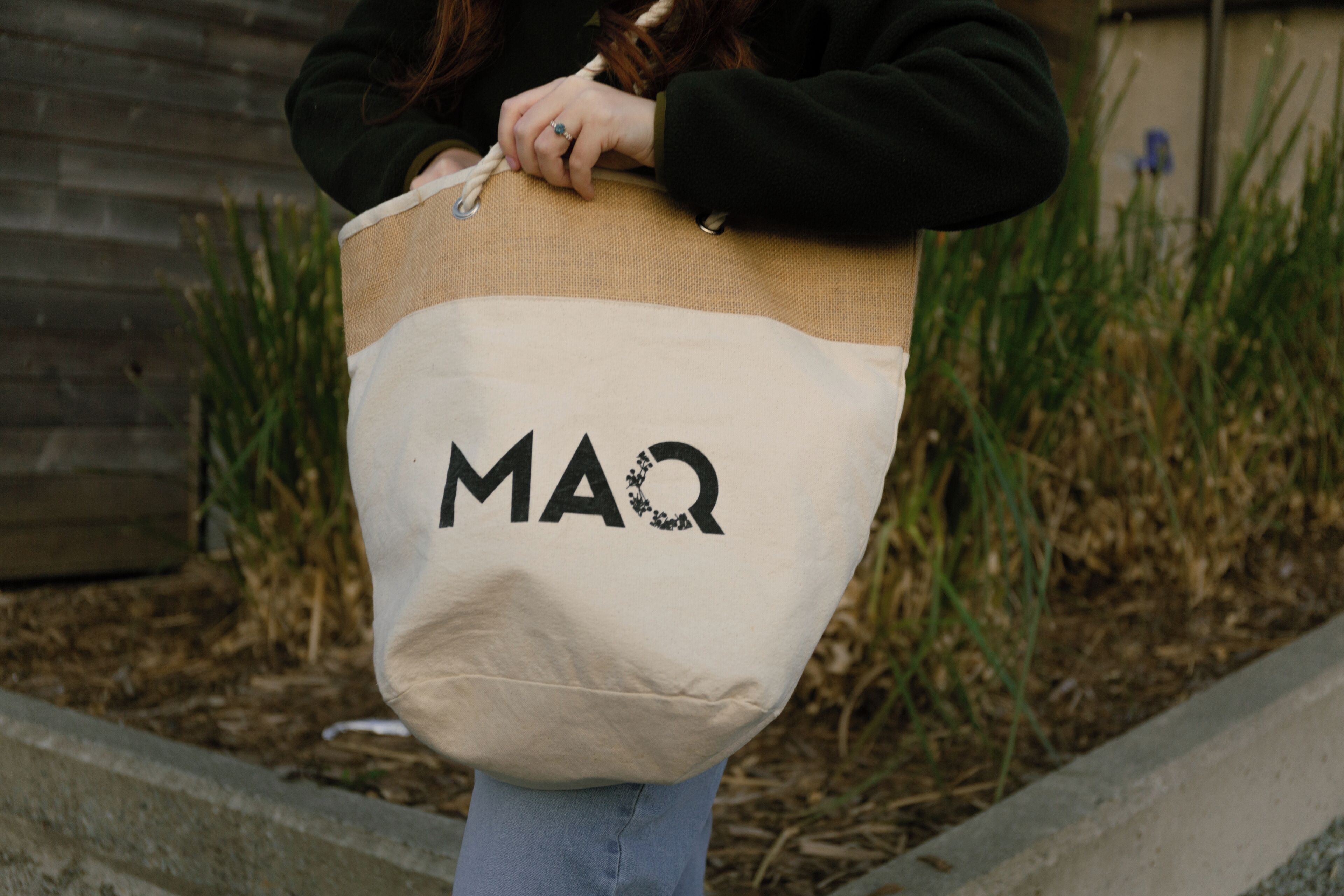 Una persona sosteniendo una bolsa de tela color beige con las letras 'MAQ' estampadas.