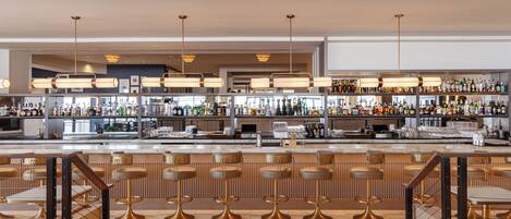 A modern bar area with multiple stools, a counter with bar tools, and a variety of bottles and glasses.