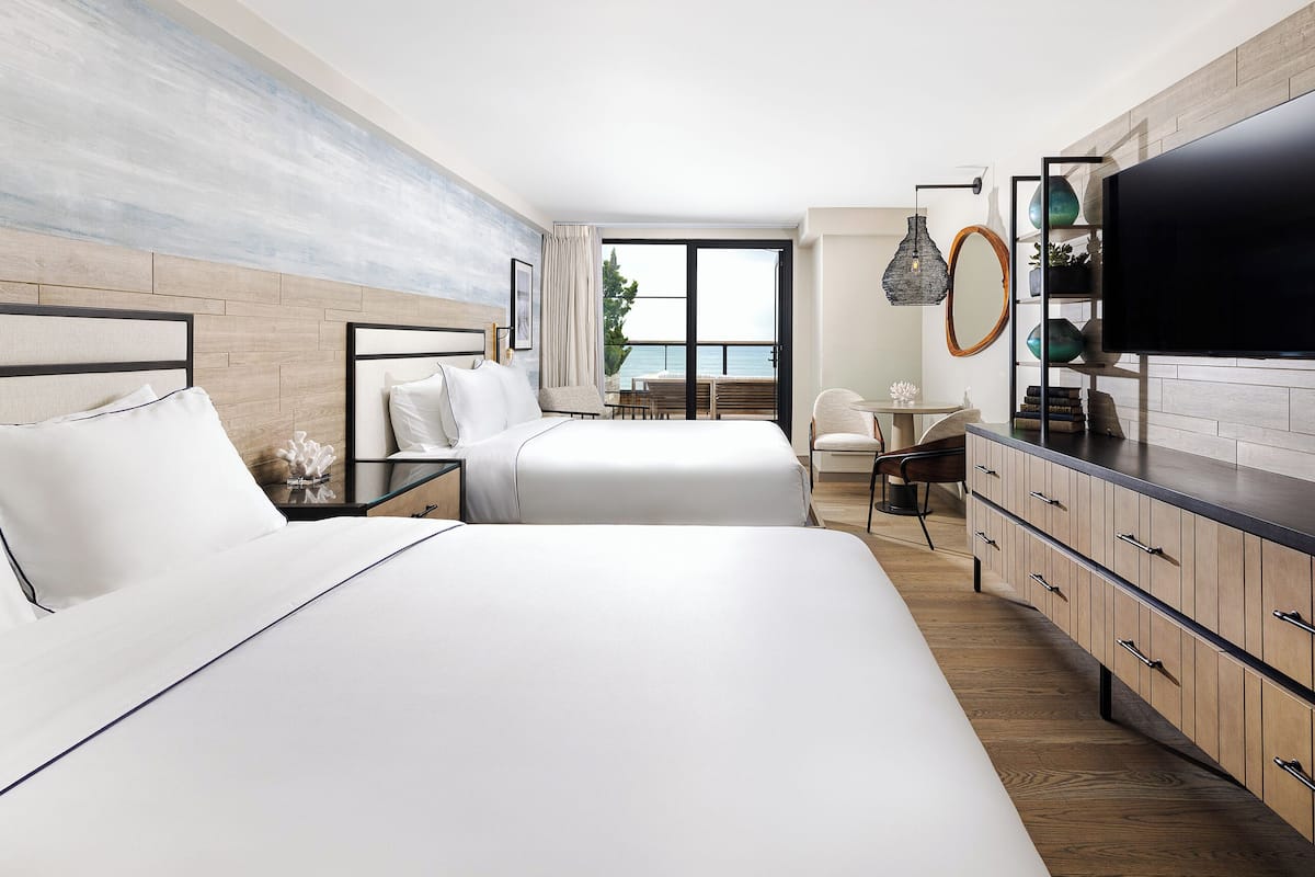 A modern hotel room with two beds, a dining area, and a large TV.