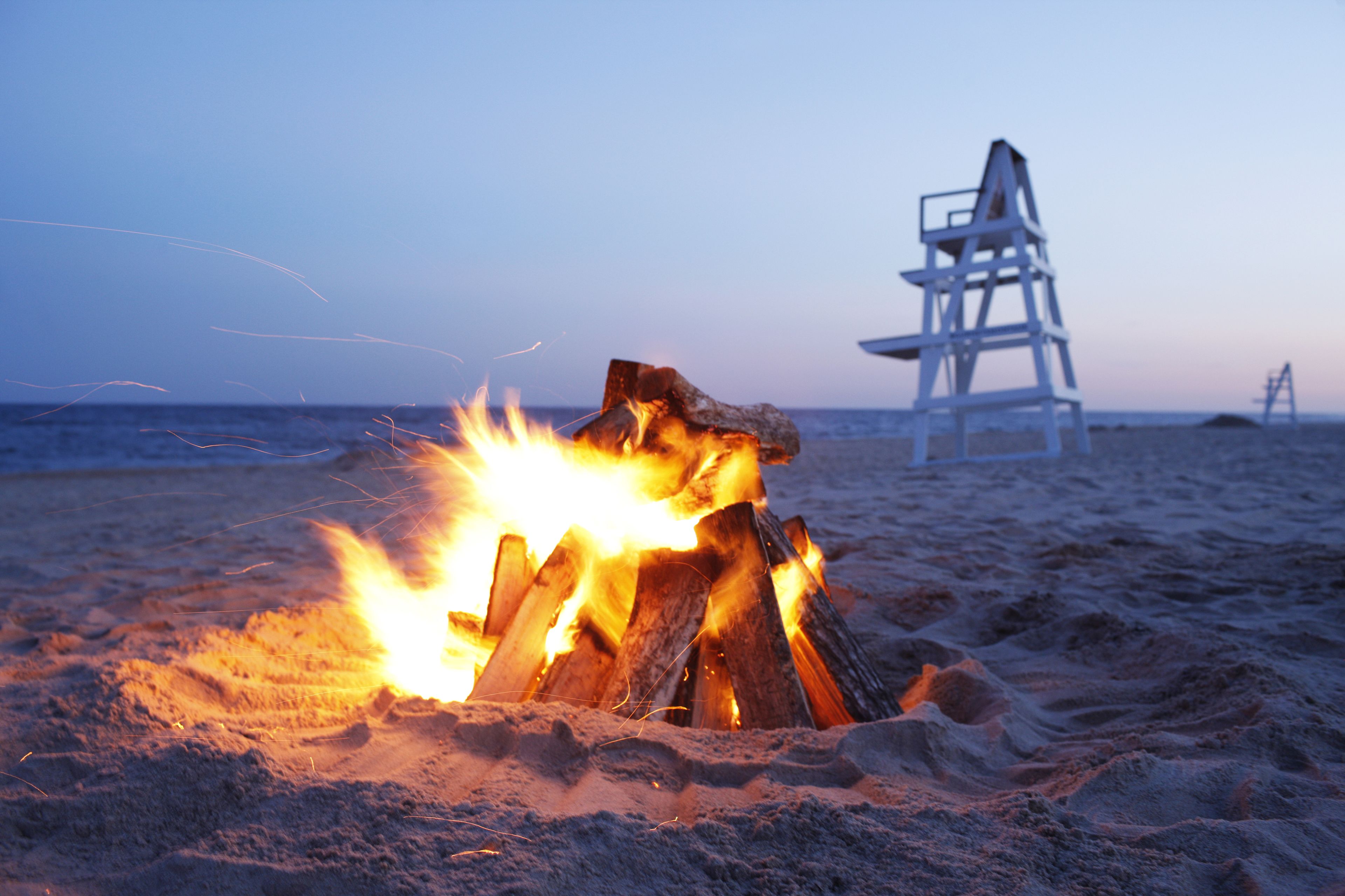 A beach scene with a fire and lifeguard chairs.