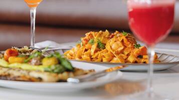 A dining table with two plates of pasta and two drinks, one orange and one red, in martini glasses.
