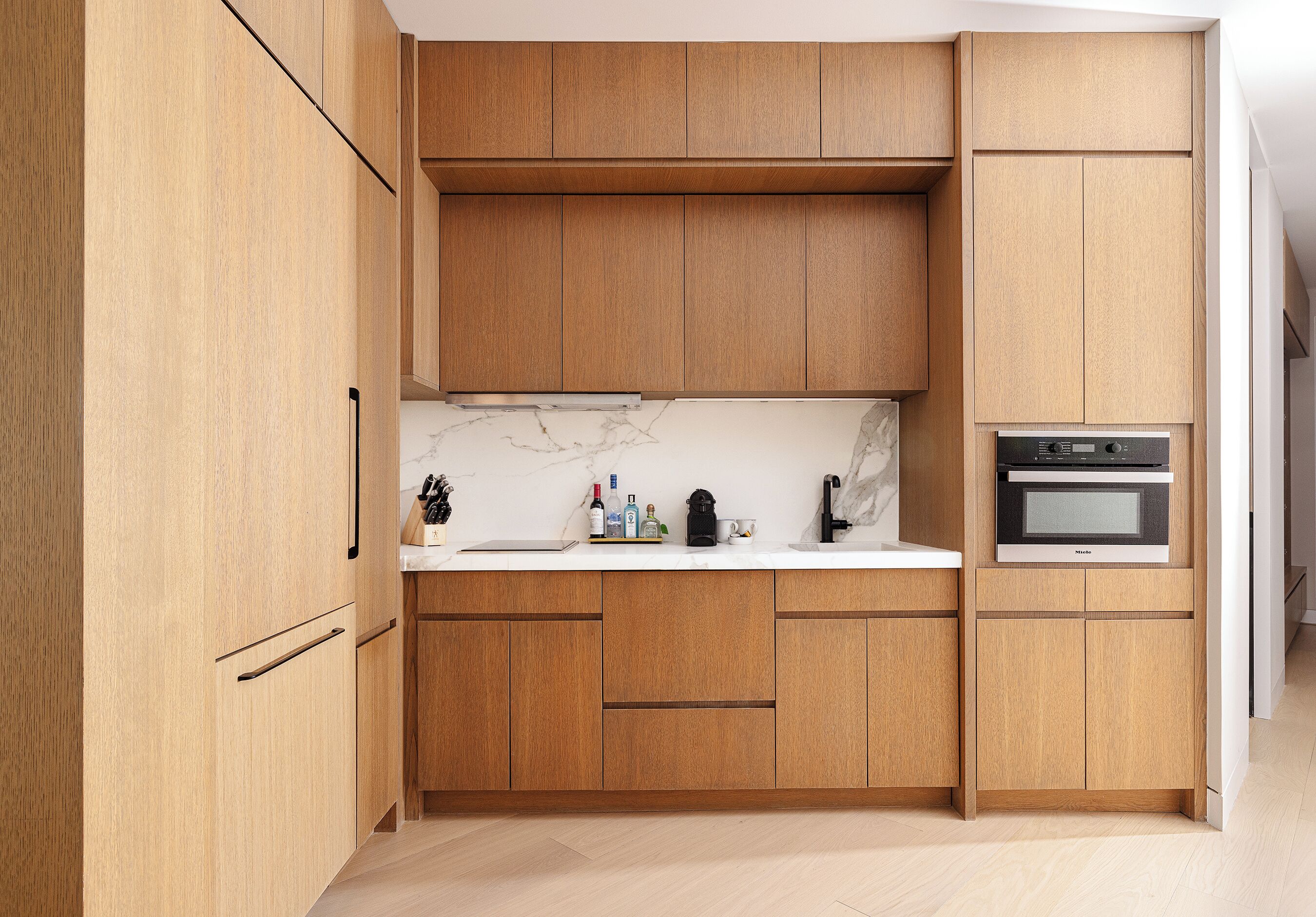 Eine moderne Küche mit Holzschränken, einer Marmor-Spritzschutzwand und einem eingebauten Backofen.