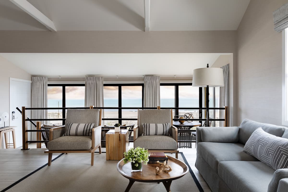 A modern living room with two armchairs, a sofa, a coffee table, and a view of the ocean.