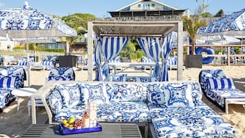 A beachside lounge area with blue and white patterned furniture, including sofas and chairs, and a table with a fruit bowl.
