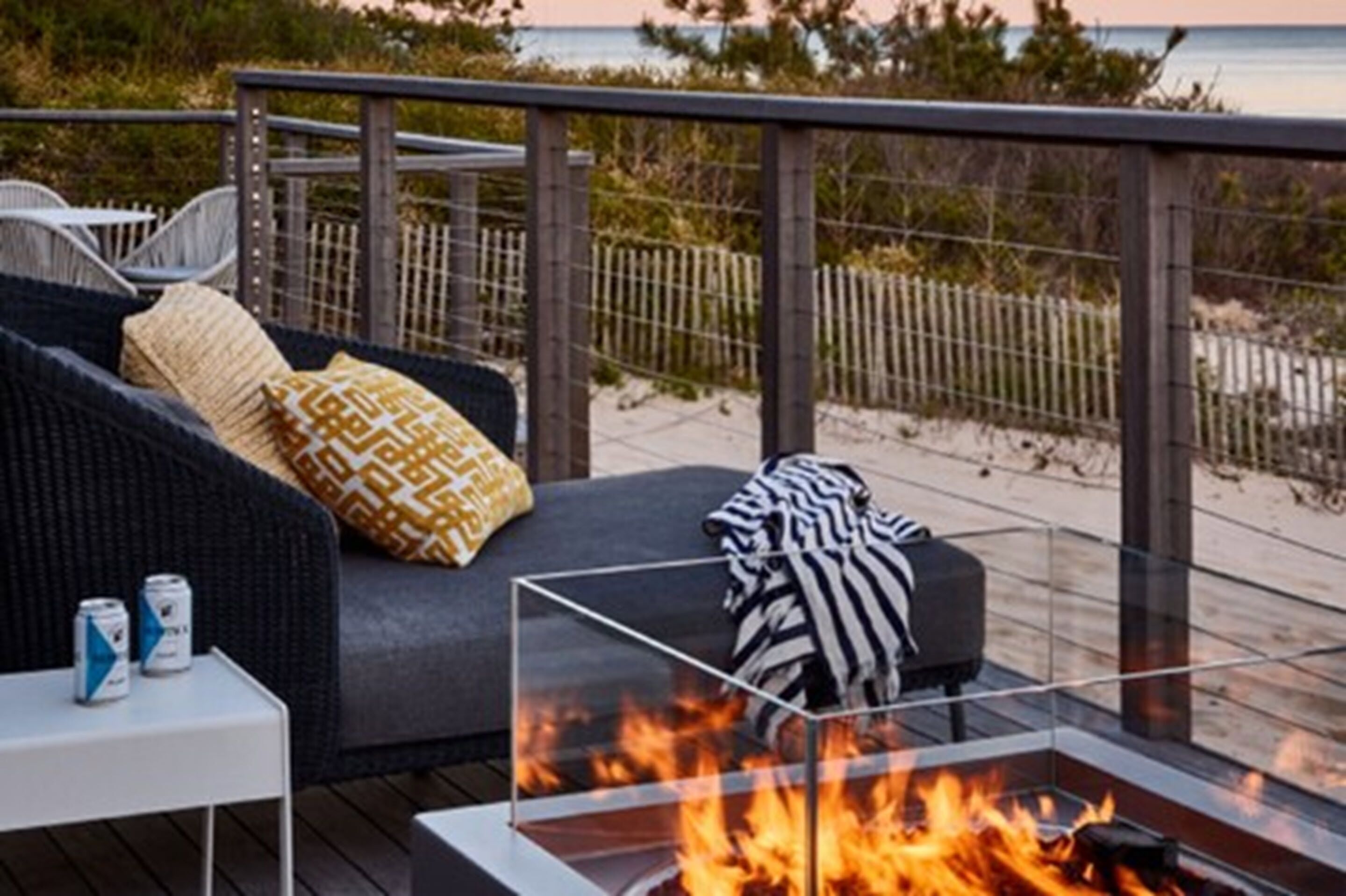 Una terraza con un brasero de vidrio, asientos exteriores y vista a la playa.