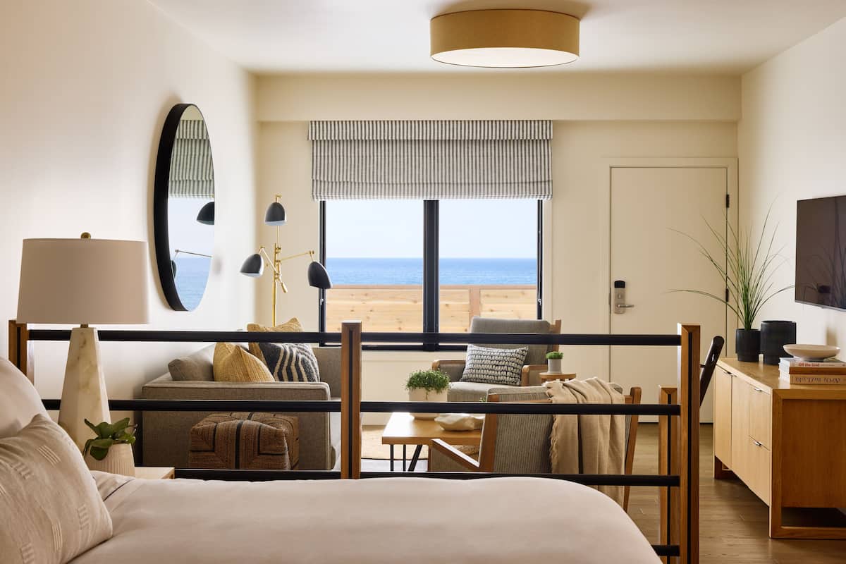 A bedroom with a view of the beach, a bed, a desk, and a chair.