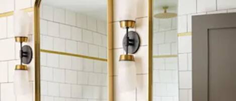 A bathroom with white tiled walls, a marble countertop, gold fixtures, and a large mirror.