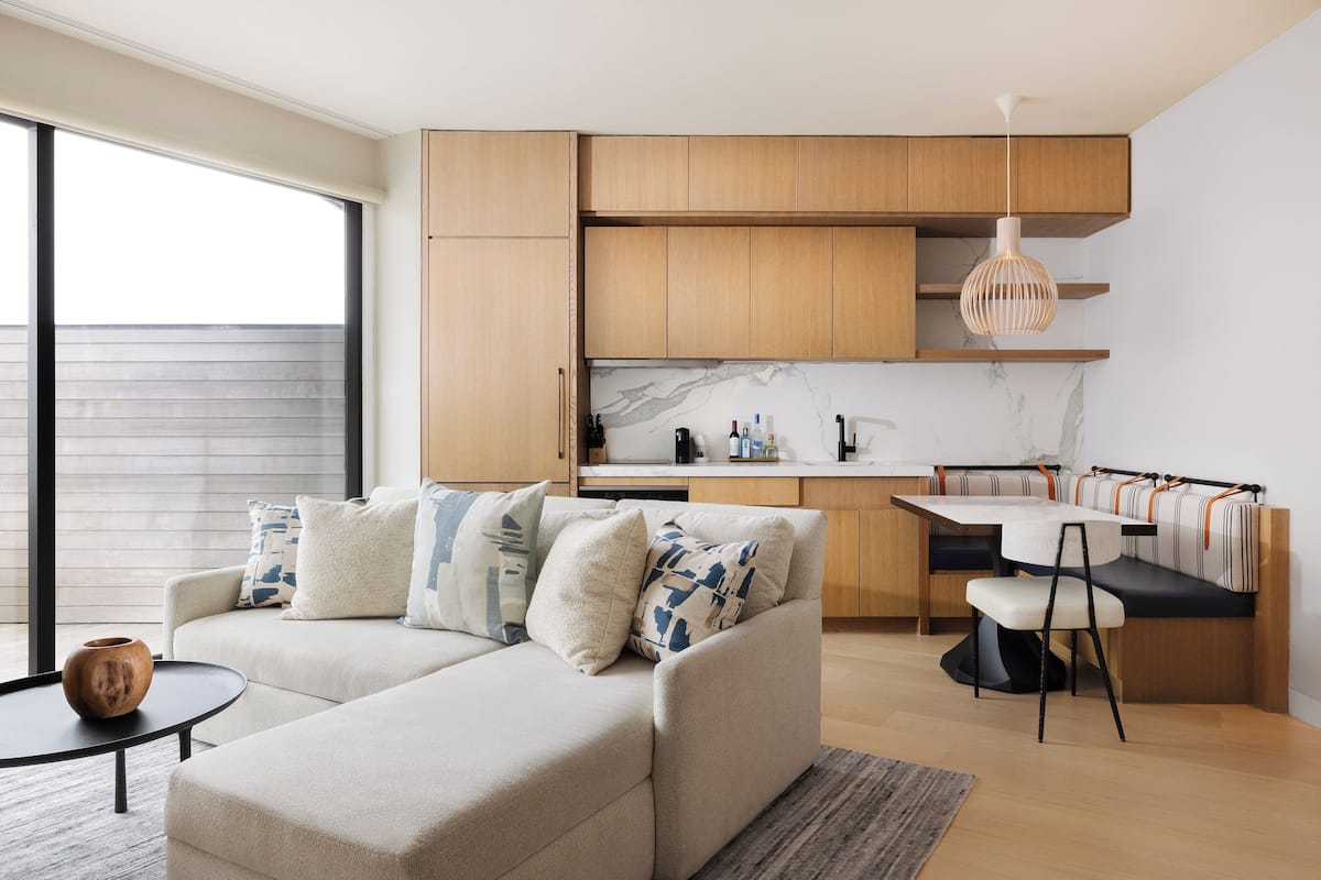 A modern living room with a sofa, coffee table, and a dining area with a bench.