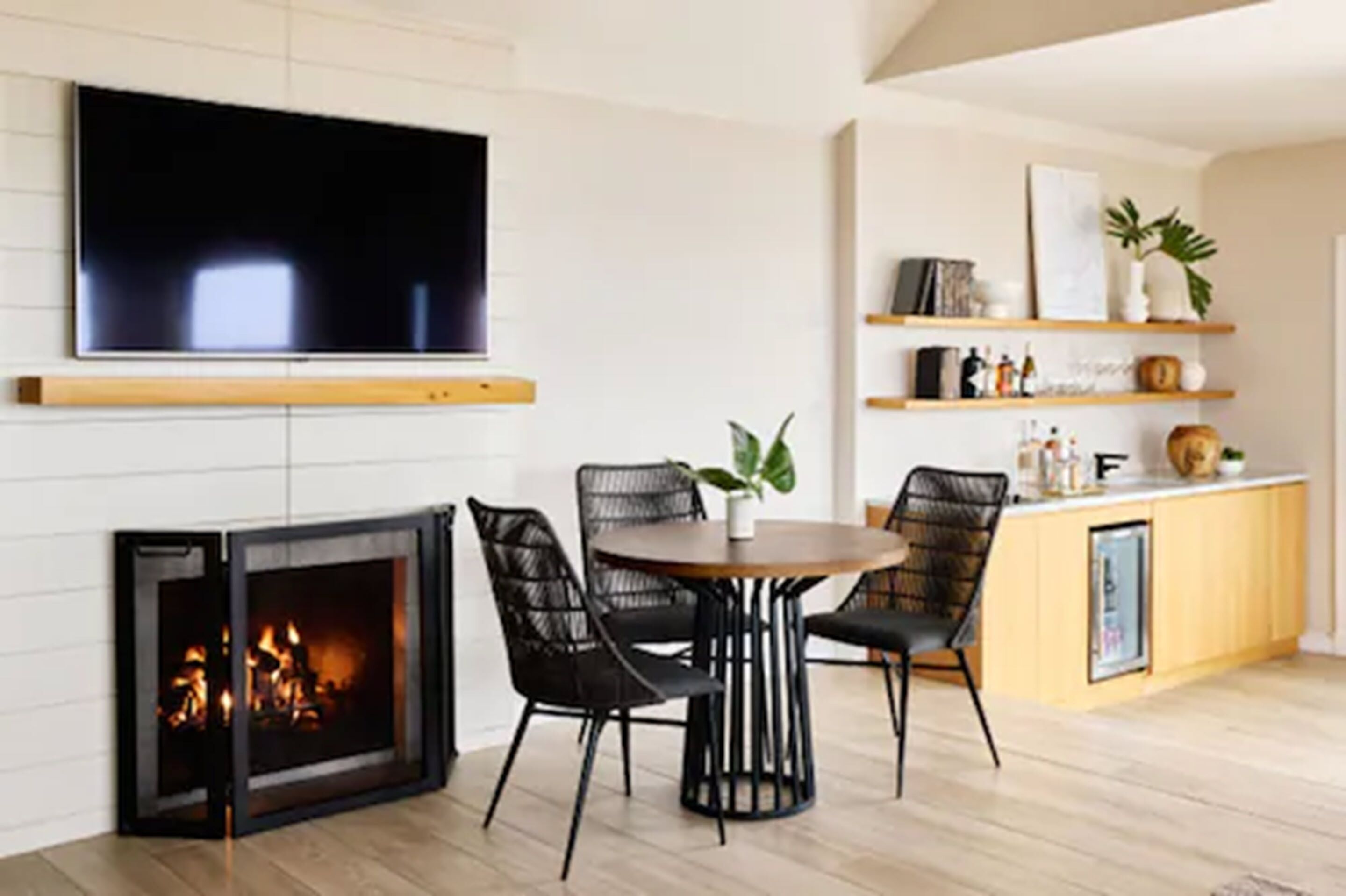A living room with a fireplace, a TV mounted on the wall, and a dining area with chairs and a table.