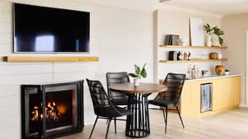 A living room with a fireplace, a TV mounted on the wall, and a dining area with chairs and a table.