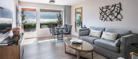 Una sala de estar moderna con un sofá gris, una mesa de centro de vidrio y un comedor con sillas y una mesa.