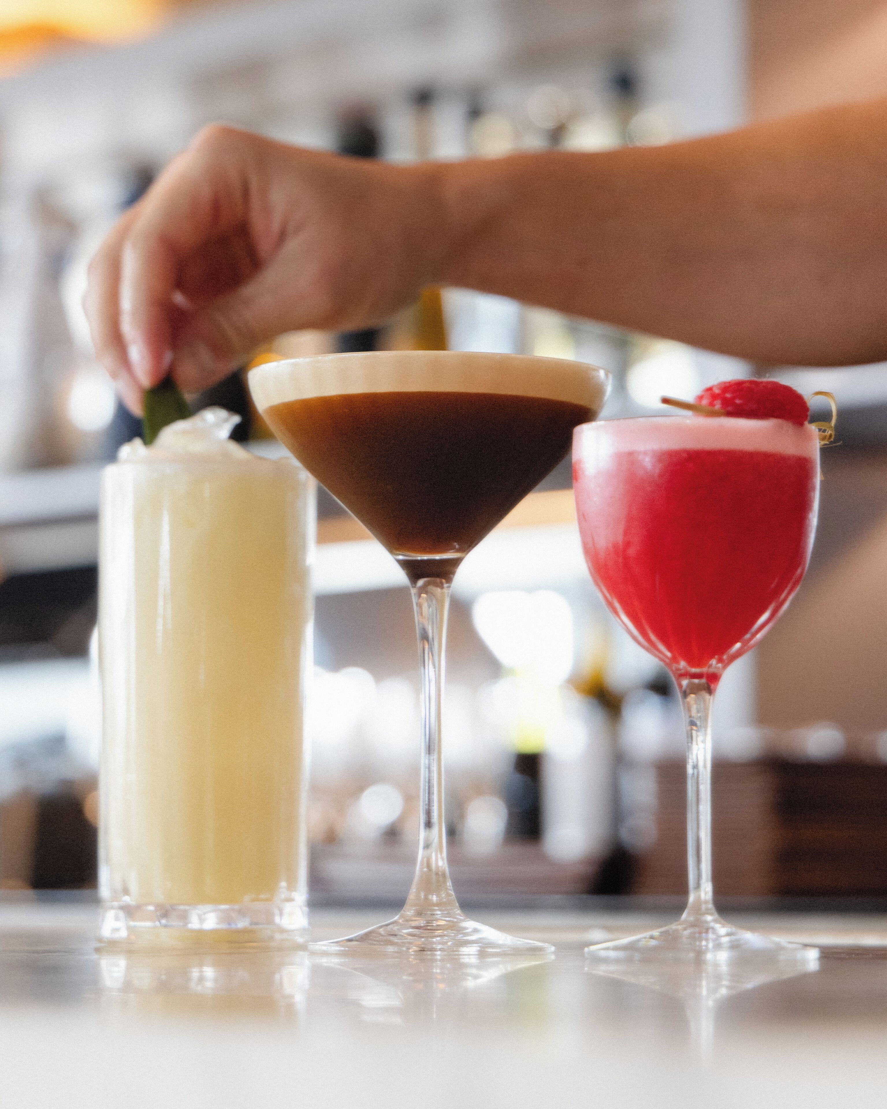 Tres bebidas diferentes en copas de martini sobre una barra.