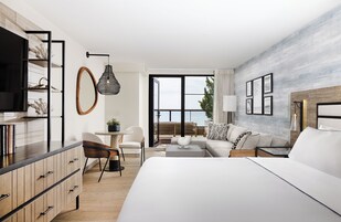 Habitación de hotel moderna con una cama grande, un escritorio, una silla, un sofá y vistas al mar.