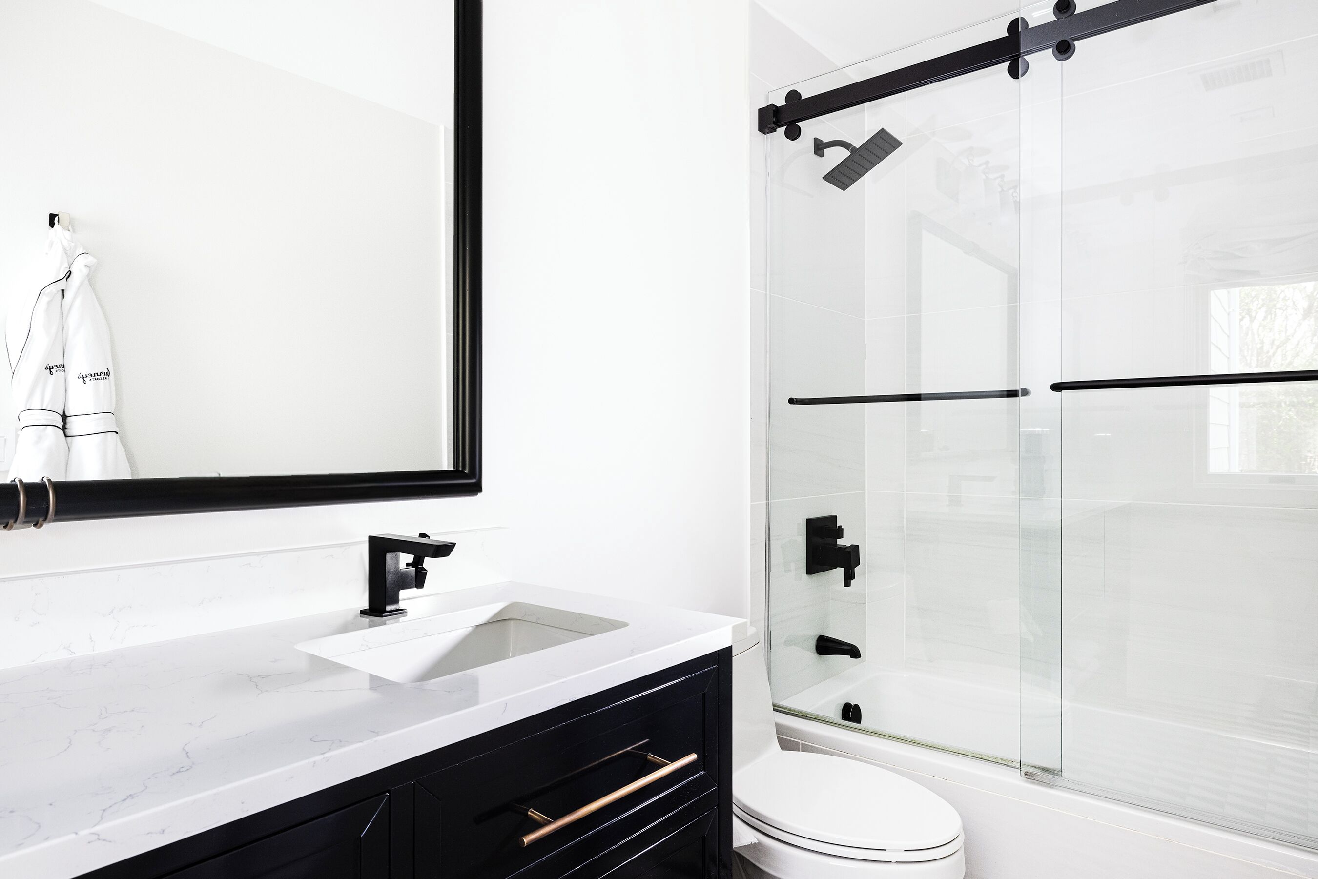 A modern bathroom with a white sink, black cabinet, and a glass shower enclosure.