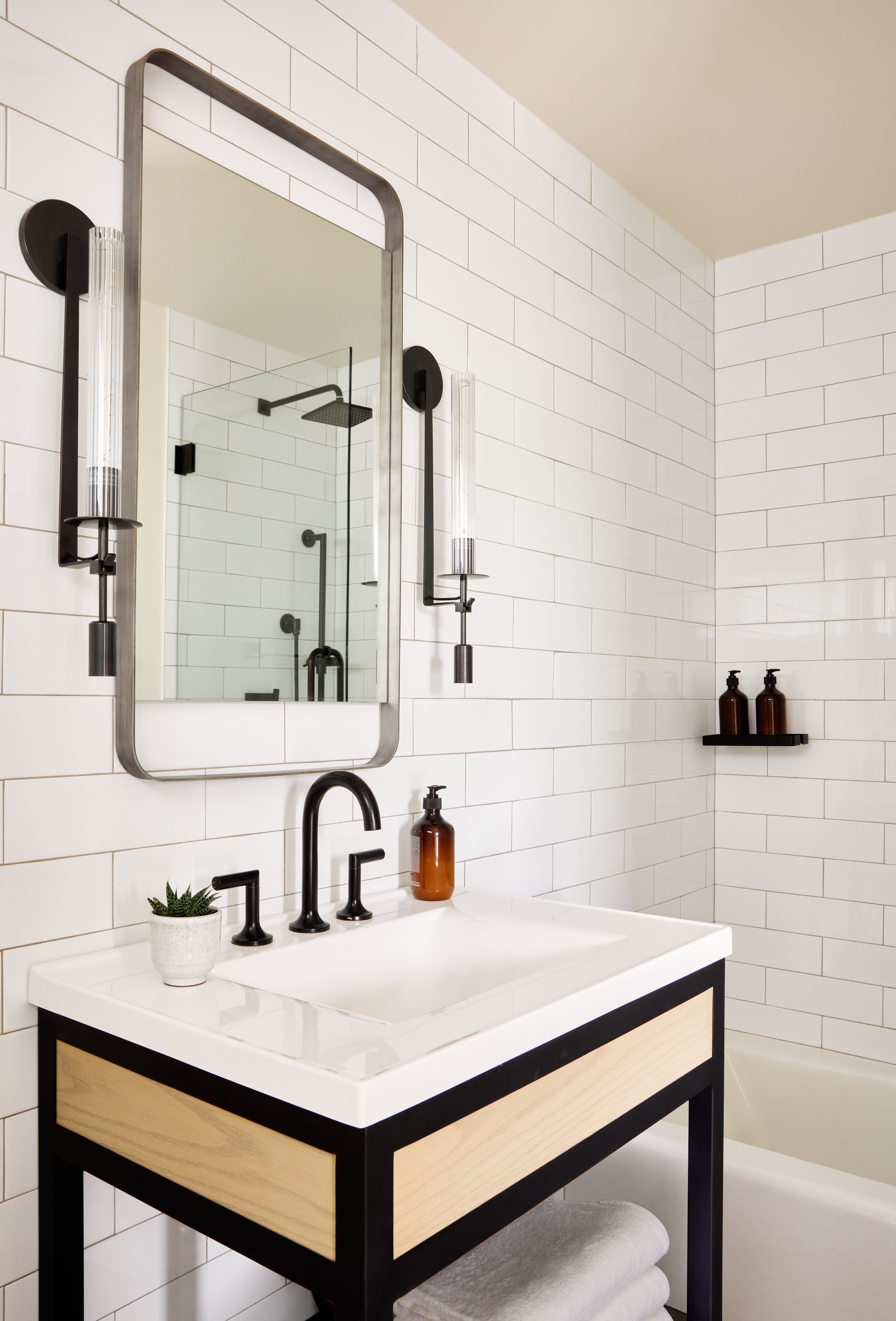 A bathroom with a white tiled wall, a large mirror, a black-framed sink, and a white countertop.