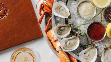 A seafood platter with oysters, lemon, and sauces on ice, accompanied by a glass of white wine and a lobster tail.