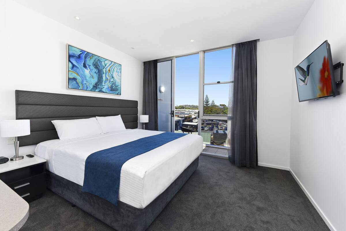 Ein modernes Hotelzimmer mit einem großen Bett, einem Flachbildfernseher, einem Gemälde und Blick auf die Stadt.