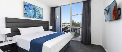 Moderni hotellihuone, jossa on suuri sänky, taulutelevisio, taulu ja näkymä kaupunkiin.