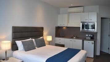 Habitación de hotel tipo estudio con cama, lámparas de noche, kitchenette con microondas y un refrigerador pequeño.