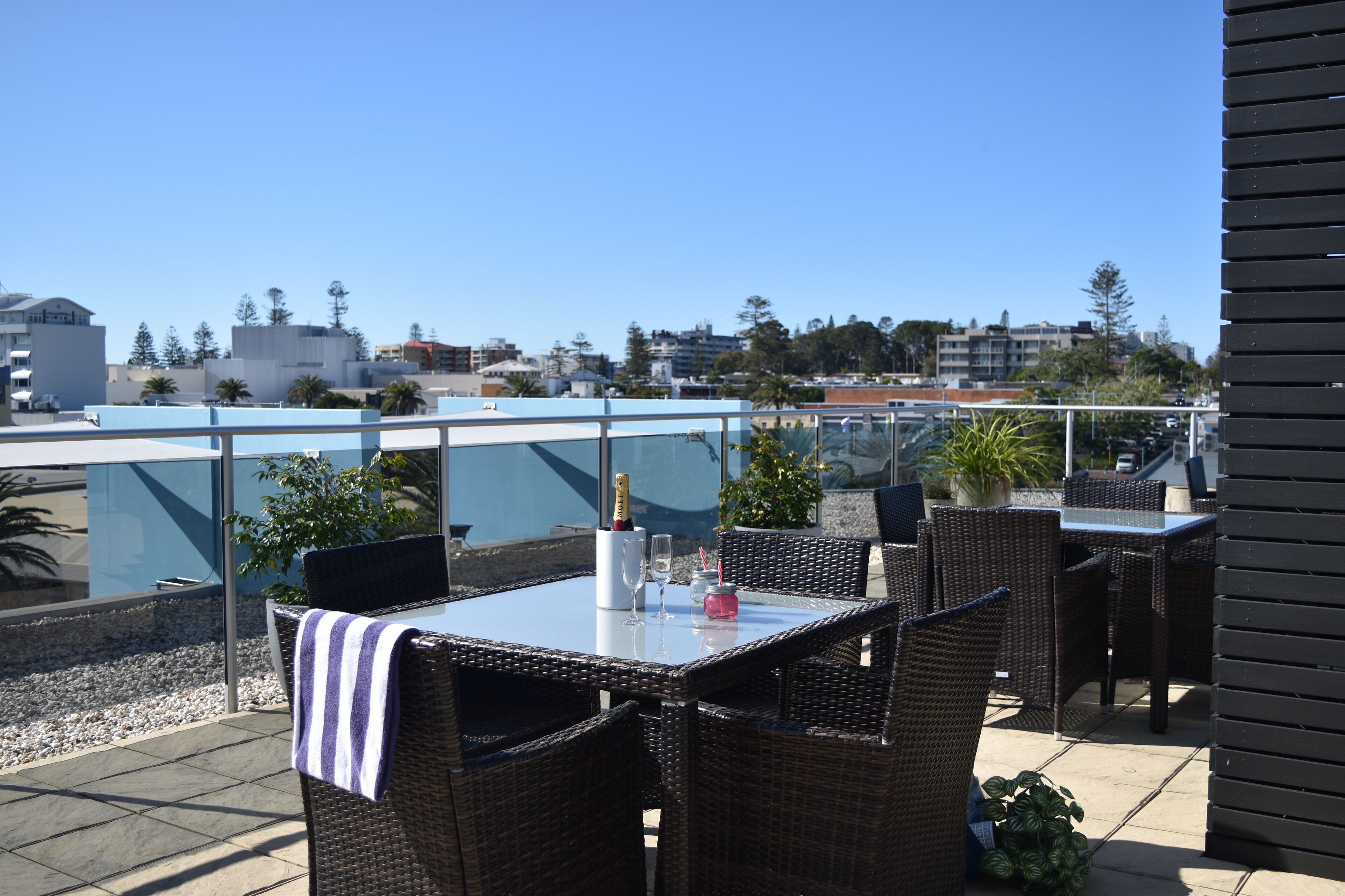 Une terrasse extérieure aménagée avec des meubles en osier, une table en verre et une vue sur le paysage urbain.