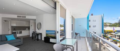 A modern apartment with a balcony, a kitchenette, a sofa, a dining table, and a TV.