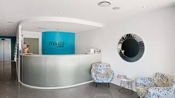 A reception area with a curved counter, a blue accent wall, two patterned chairs, and a round mirror on the wall.