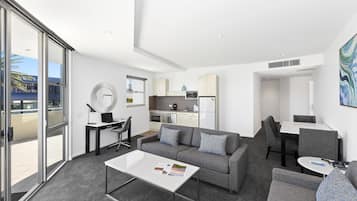 A modern living room with a sofa, coffee table, and dining area. A kitchen is visible in the background.