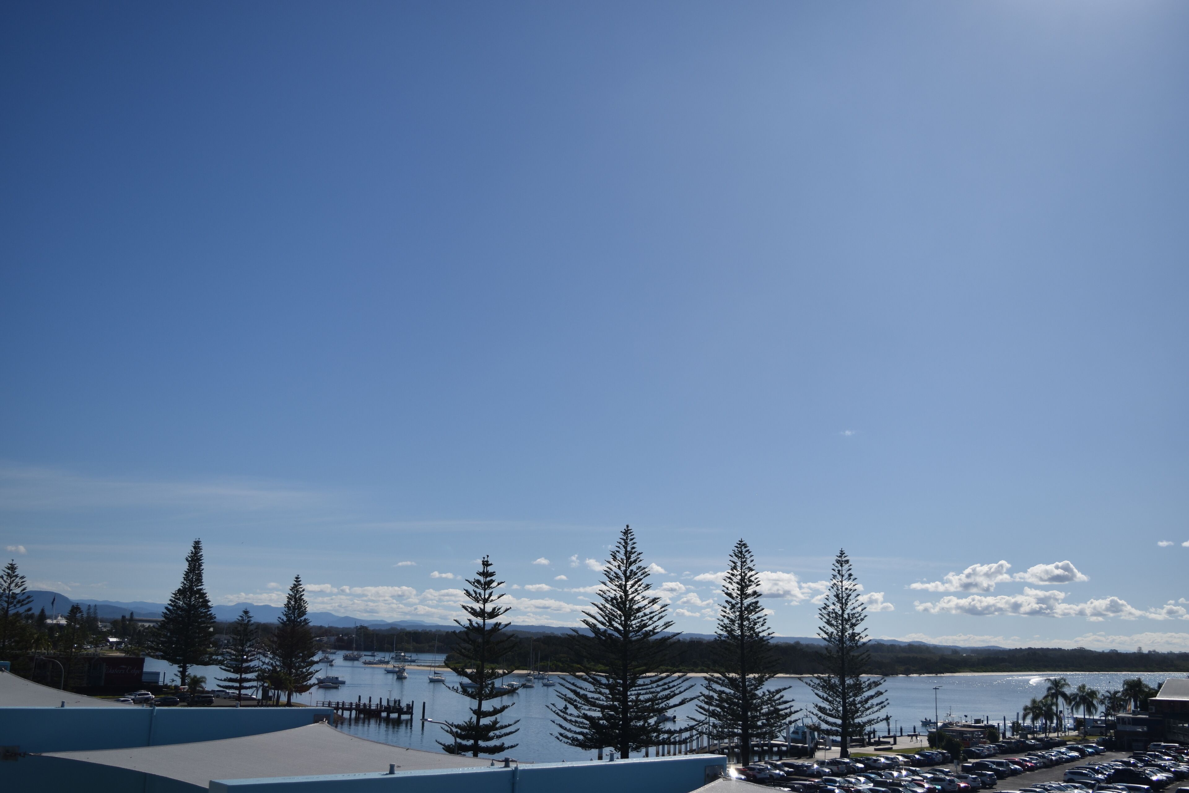 A parking lot with several cars, a marina with boats, and a clear blue sky.