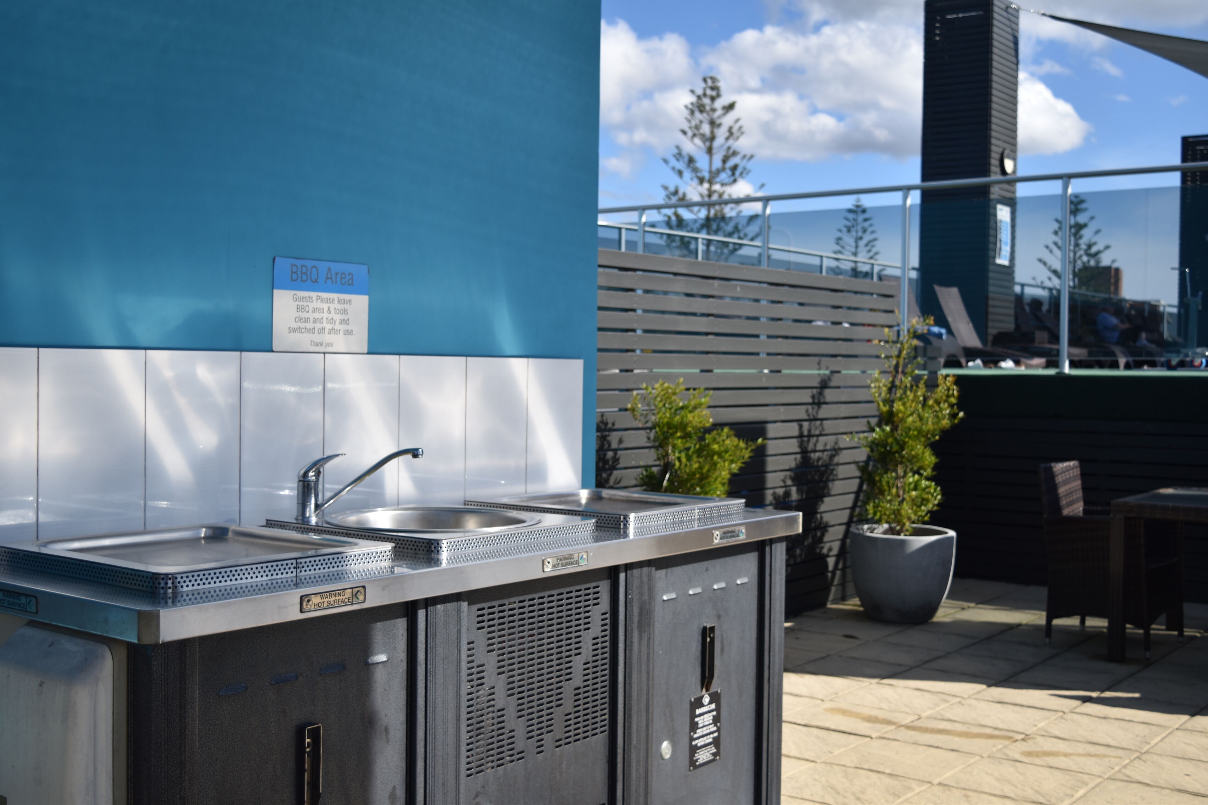 Un espace barbecue équipé d’éviers en acier inoxydable et d’un panneau indiquant aux clients qu’ils doivent nettoyer et ranger les lieux après utilisation.