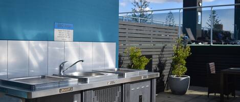 A BBQ area with stainless steel sinks and a sign instructing guests to clean and tidy up after use.