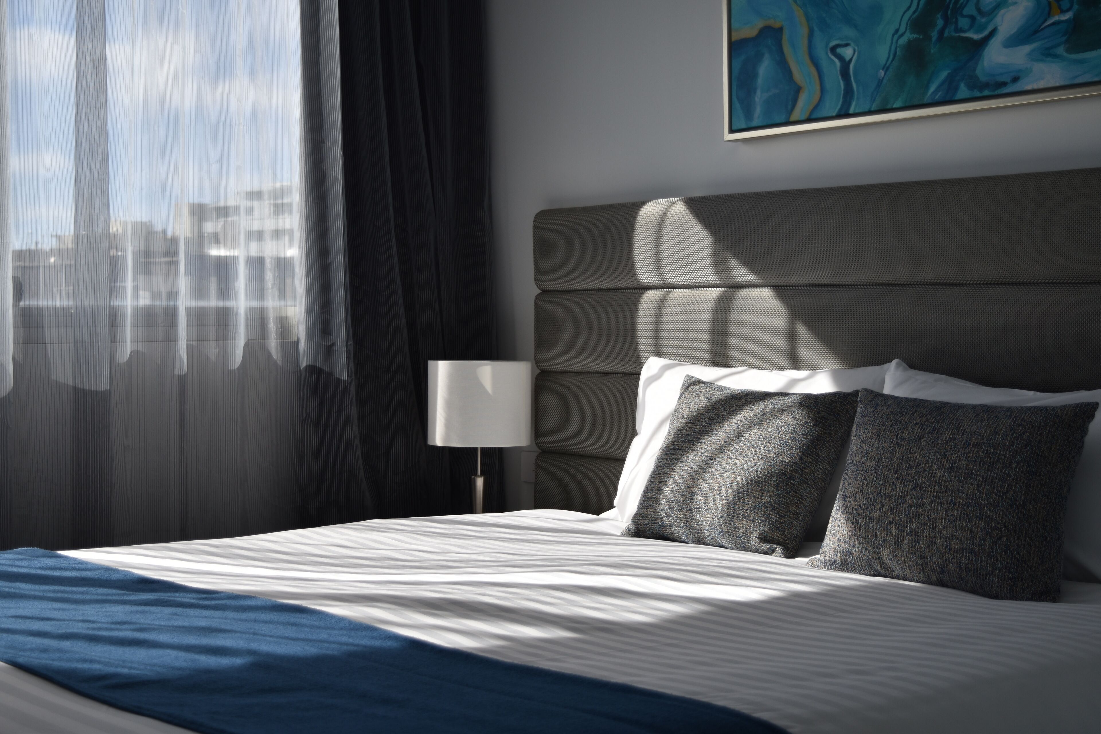 A neatly made bed with a blue blanket, a grey headboard, and two grey pillows.