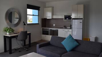 A 2 bedroom living room/kitchen with a modern design, including a sofa, a desk, a chair, a mirror, cabinets, and a kitchen with appliances.