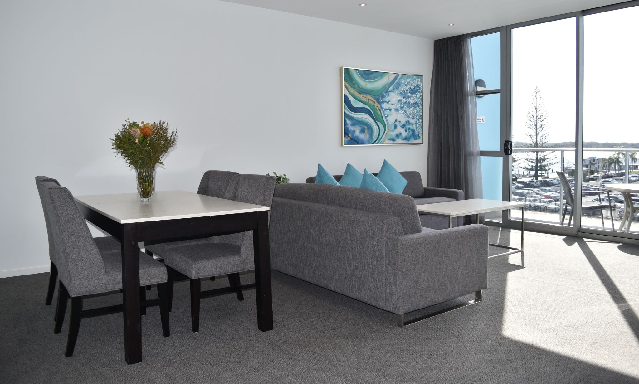 Salón comedor de un dormitorio, con una mesa de comedor, sofá gris y un ventanal con vista al estacionamiento.