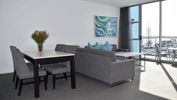 Salón comedor de un dormitorio, con una mesa de comedor, sofá gris y un ventanal con vista al estacionamiento.