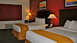 A hotel room with two beds, a large window with curtains, a painting on the wall, and two bedside lamps. - Landmark Inn Fort Irwin (Fort Irwin)