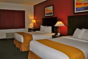 A hotel room with two beds, a large window with curtains, a painting on the wall, and two bedside lamps. - Landmark Inn Fort Irwin (Fort Irwin)