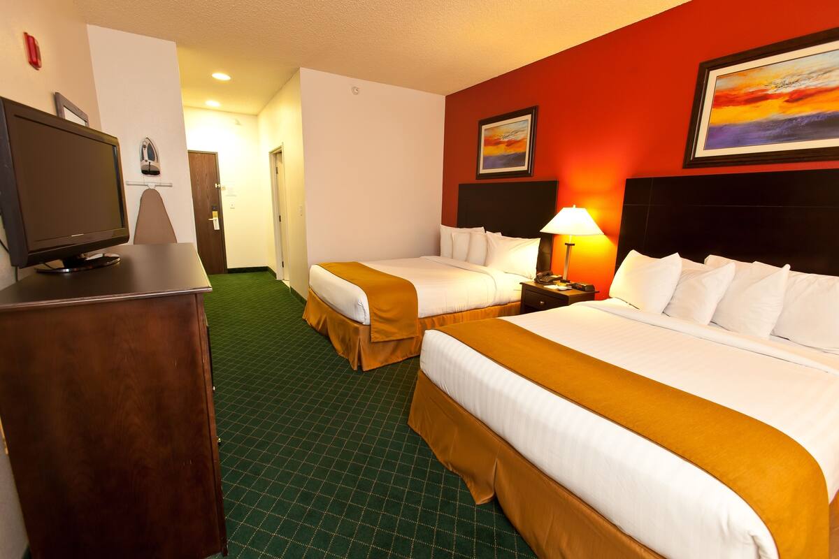 A hotel room with two beds, a television, a desk, and a painting on the wall.