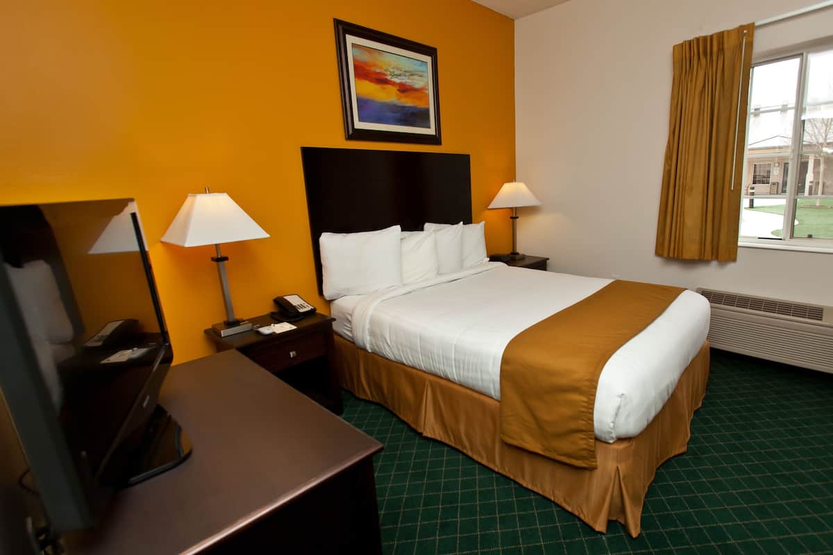 A hotel room with a bed, two bedside tables with lamps, a desk with a telephone, a painting on the wall, and a window with curtains.