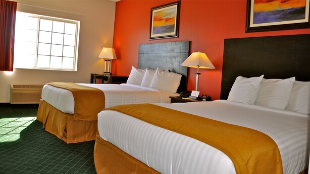 A hotel room with two beds, a large window, a painting, and a nightstand with a lamp. - Landmark Inn Fort Irwin (Fort Irwin)